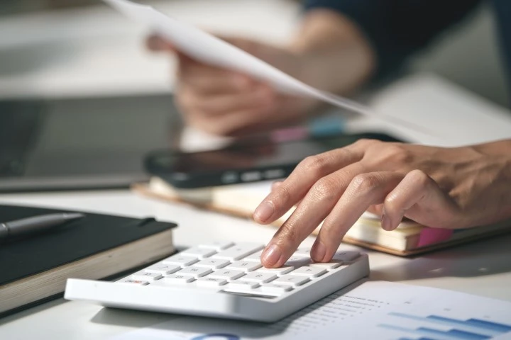 A hand using a calculator at a desk.